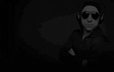 a man wearing sunglasses and headphones is standing with his arms crossed in a black and white photo .