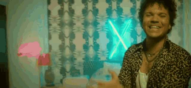 a man in a leopard print shirt is dancing in a bedroom with a neon sign behind him .