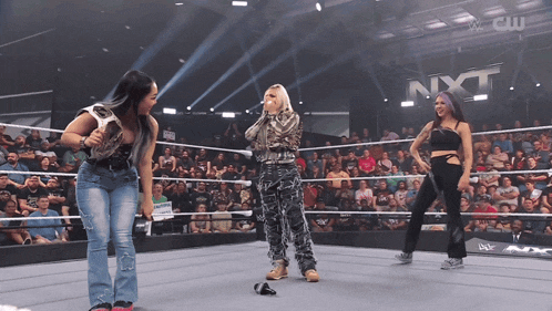 three women are standing in a wrestling ring with nxt written on the wall behind them