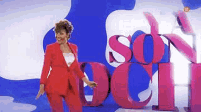 a woman in a red suit is standing in front of a large pink sign that says son och .