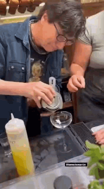 a man is pouring a drink into a glass while a woman looks on .