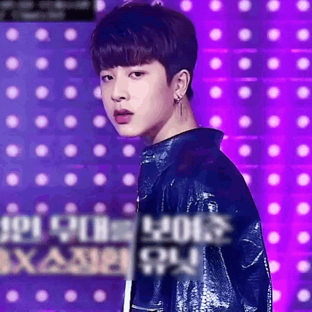 a young man wearing earrings and a blue jacket stands in front of purple lights