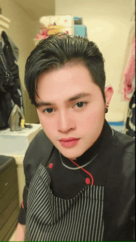 a man wearing a black shirt and striped apron is taking a selfie