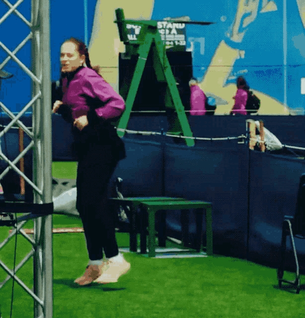 a woman in a purple jacket is jumping in front of a sign that says stand sta