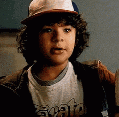 a young boy with curly hair wearing a hat and a t-shirt .