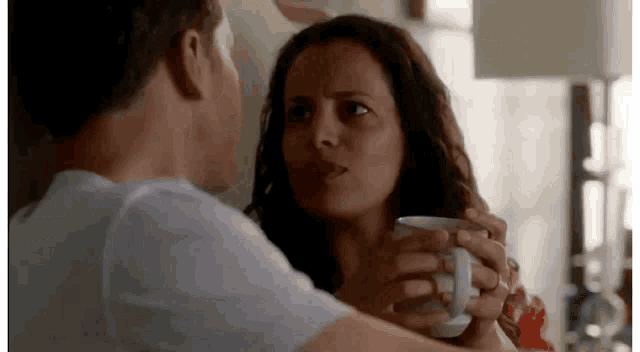 a man and a woman are looking at each other while the woman is holding a coffee mug .