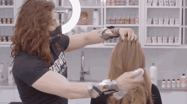 a woman with long hair is getting her hair done by a hairdresser wearing a shirt that says ' everything ' on it