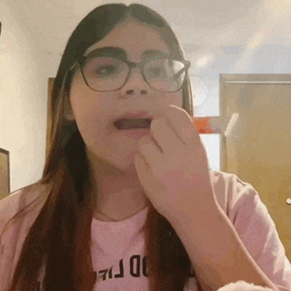 a girl wearing glasses and a pink shirt is eating a piece of food .