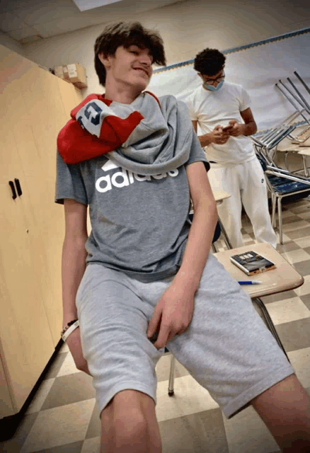 a boy wearing a gray adidas shirt sits on a desk