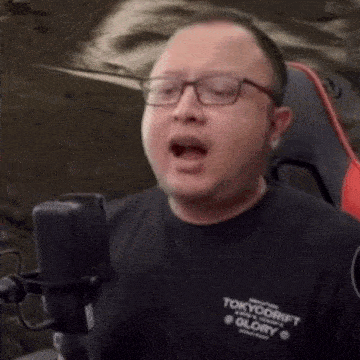a man wearing glasses is singing into a microphone while sitting in a chair .