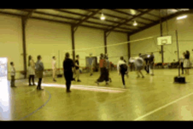 a group of people playing volleyball in a gym with a basketball hoop in the background