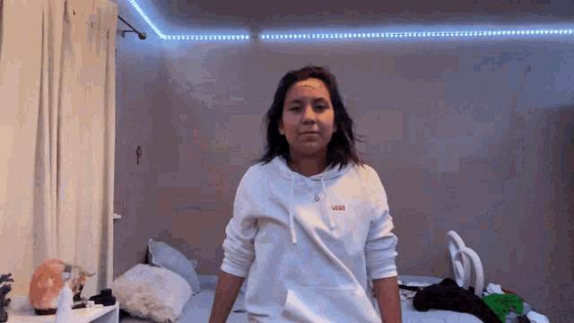 a woman wearing a white vans hoodie is standing in a bedroom