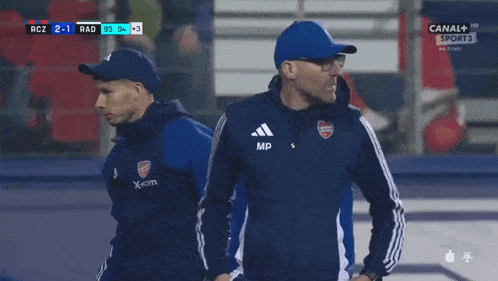 a man in a blue hat stands in front of a scoreboard that says canal sport