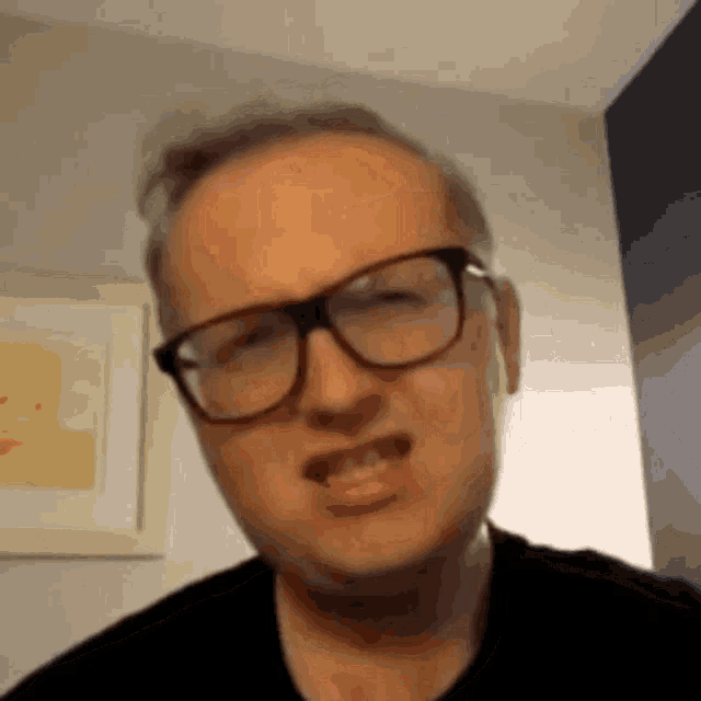 a man wearing glasses and a black shirt making a funny face