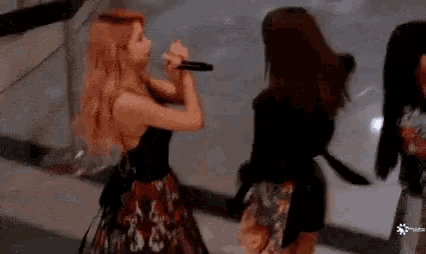 a woman in a black dress is singing into a microphone while two other women look on .