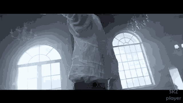 a man in a white shirt is standing in front of arched windows with srz player written on the bottom of the screen