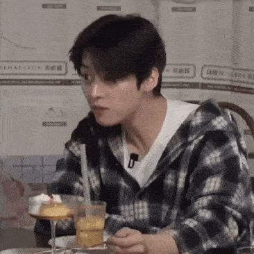 a young man in a plaid shirt is sitting at a table with a glass of orange juice and a dessert .