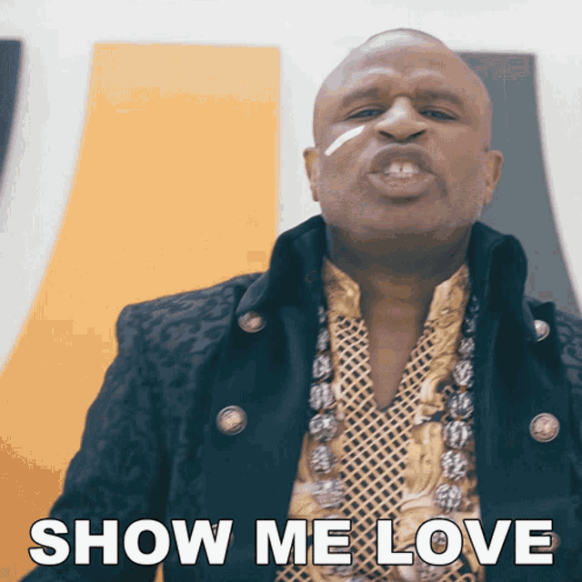 a man in a black jacket and gold shirt says " show me love "