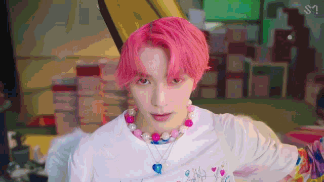 a young man with pink hair is wearing a white shirt and a colorful necklace .