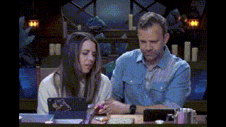 a man and a woman are sitting at a table looking at a laptop .