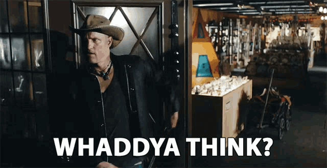 a man in a cowboy hat is standing in a dark room with the words whaddya think below him