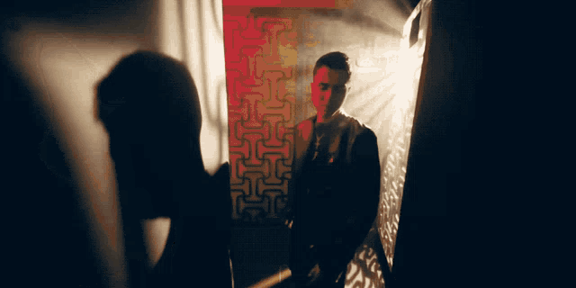 a man in a suit stands in front of a red wall