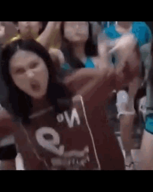 a woman is standing in front of a crowd of people wearing a brown shirt .