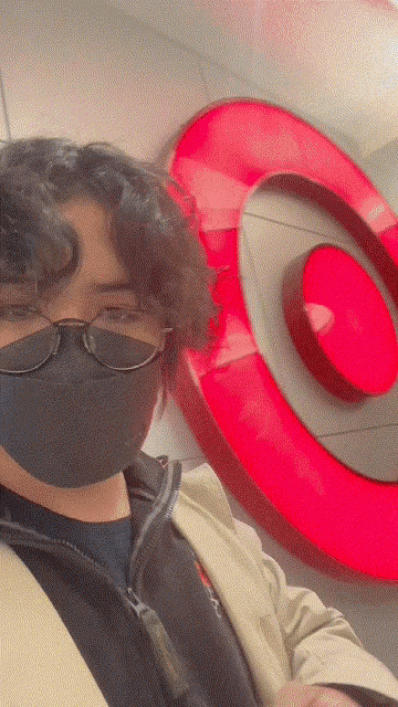a man wearing a black mask and glasses stands in front of a target sign