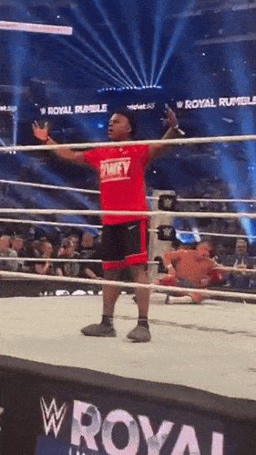 a man in a red shirt stands in a wrestling ring with the words royal rumble in the background