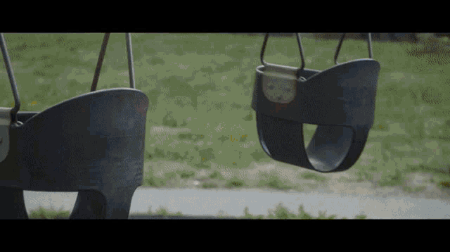 two black swings are hanging in the grass