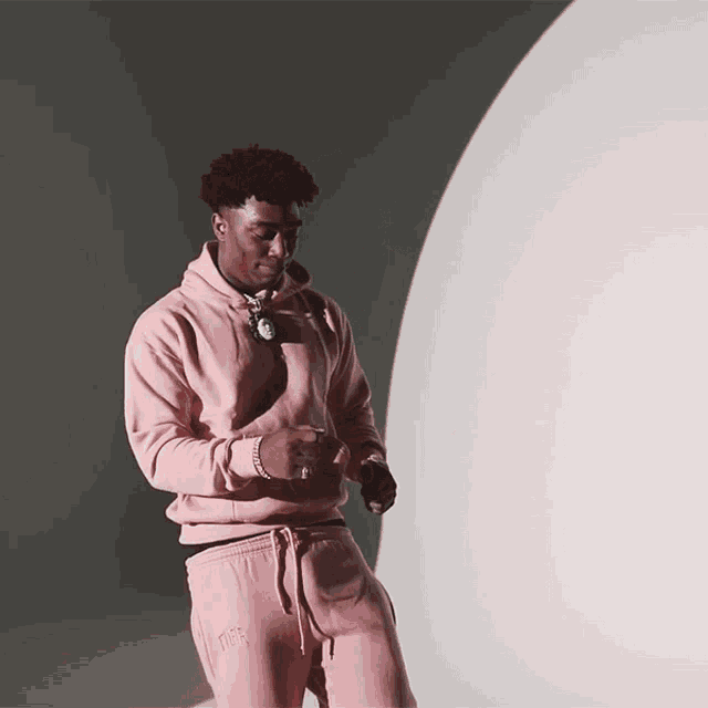a man in a pink hoodie and pink sweatpants stands in front of a white sphere