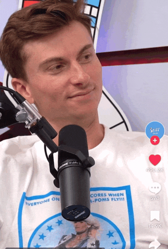 a man sitting in front of a shure microphone with a shirt that says everyone on cores when poms fly
