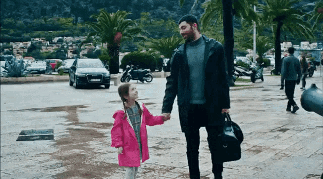 a man holding a little girl 's hand while walking down a street