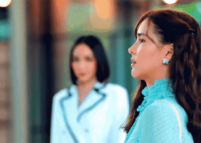 a woman in a blue dress stands next to another woman in a white suit