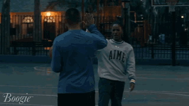 a woman wearing a aime sweatshirt is waving at a man holding a basketball