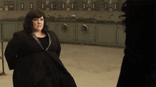 a woman in a black coat is standing next to a woman in a black dress in a kitchen .
