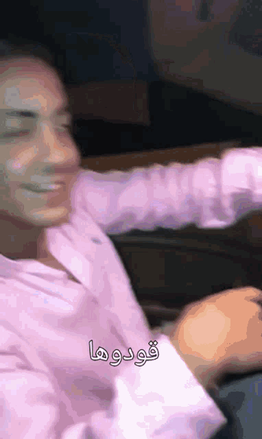 a man in a pink shirt is smiling in a blurry photo with arabic writing