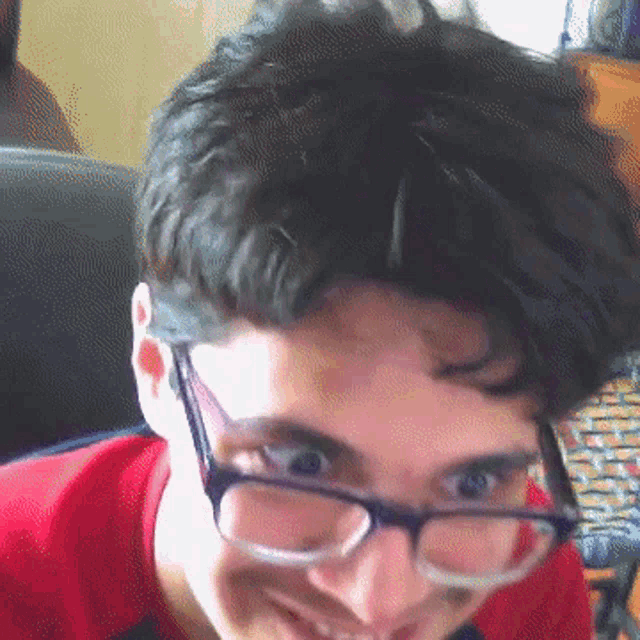 a young man wearing glasses and a red shirt smiles