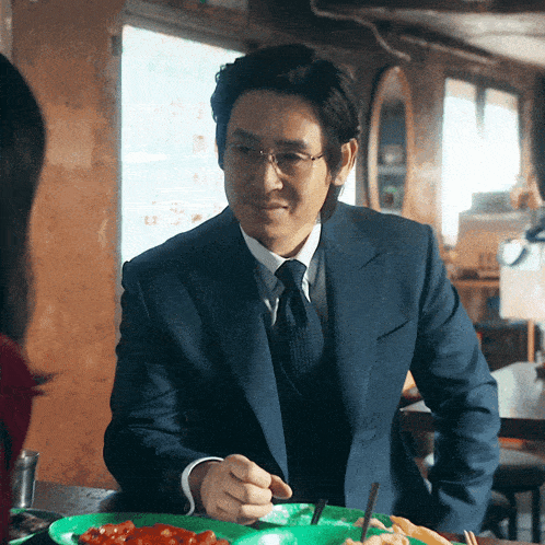 a man in a blue suit and tie is eating a plate of food