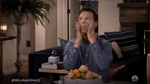 a man sitting on a couch with his hands on his face and a bowl of fruit on the table .