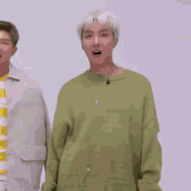 a man wearing a green sweater is standing next to another man wearing a yellow and white striped shirt .