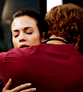 a woman in a red shirt is hugging a man in a maroon shirt
