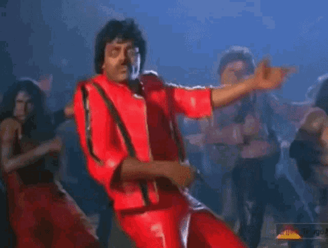 a man in a red jacket is dancing in front of a group of dancers .
