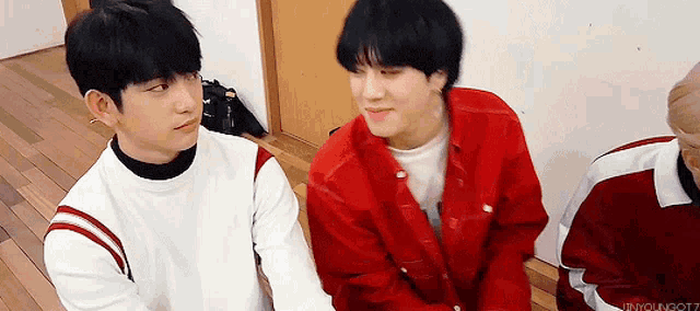 two boys are sitting next to each other on a wooden floor .