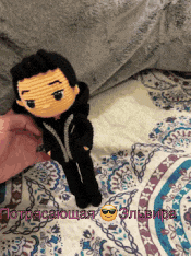 a person is holding a crocheted doll on a bed with russian writing on it
