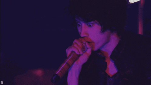 a man is singing into a microphone with a purple light behind him that says d