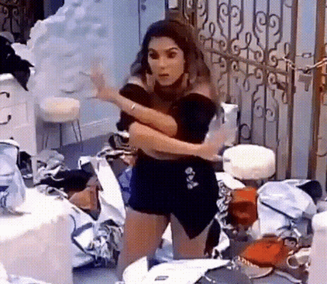 a woman in a black dress is standing in a room with a lot of bags on the floor