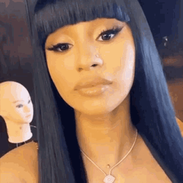 a woman with long black hair and bangs is wearing a necklace and a nose ring .