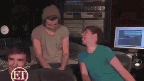 a group of men are sitting in front of a computer in a recording studio and laughing .