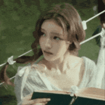 a woman with pigtails is reading a book while standing next to a rope .